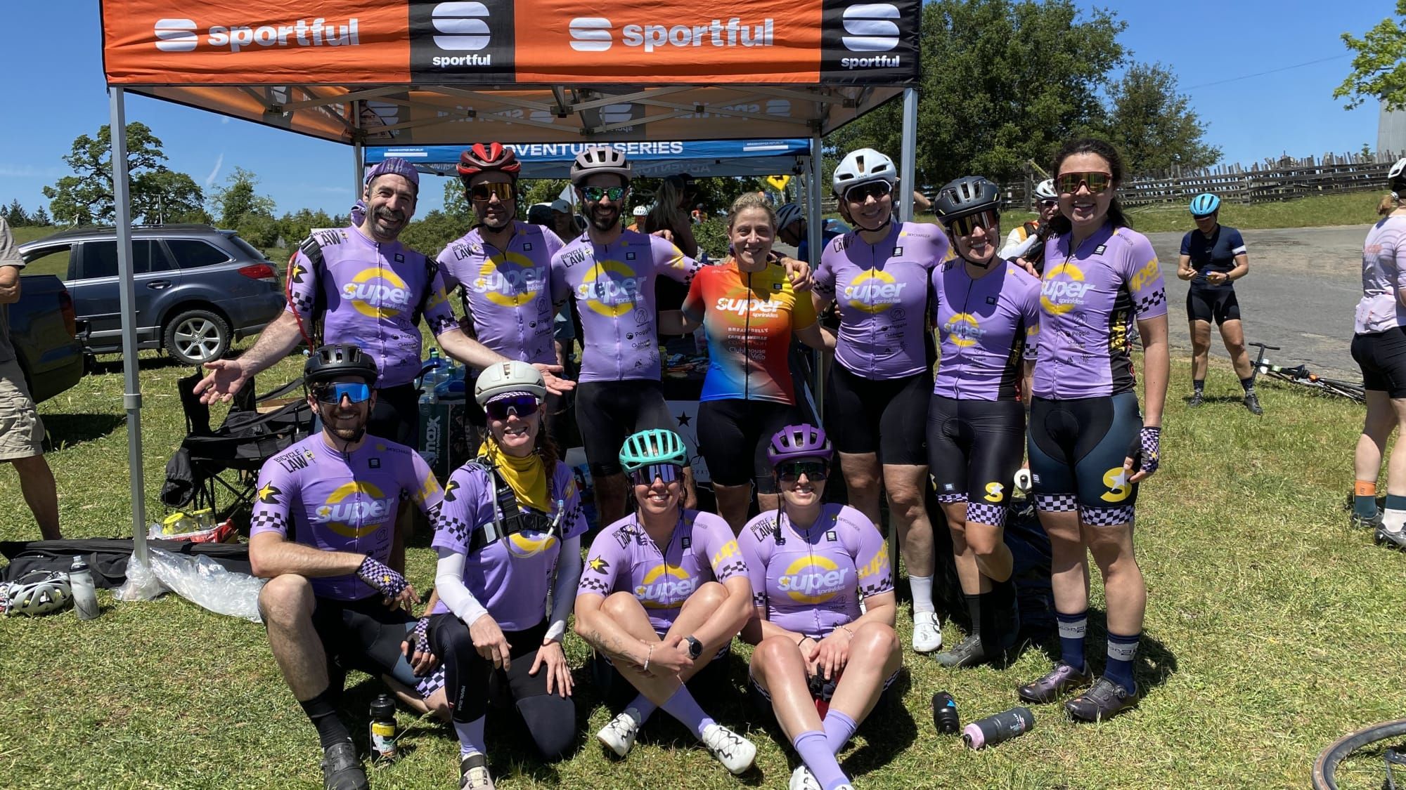 The Super Sprinkles squad in lavender team kit, grouped under the team tent at a race.